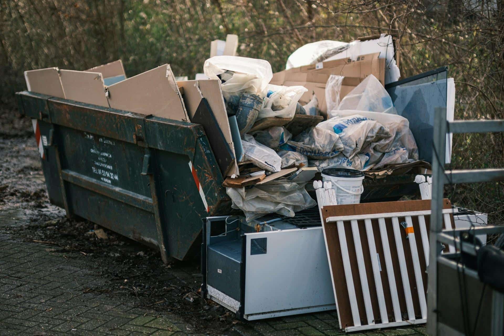 An overflowing dumpster with scattered trash and discarded items around it.