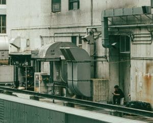 A person sits amidst industrial machinery outdoors.