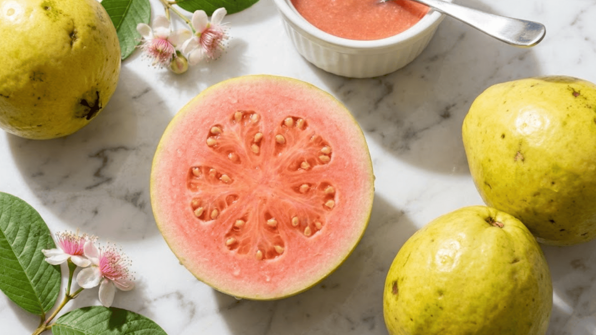 pink guava halved revealing rosy flesh and seeds on white marble surface