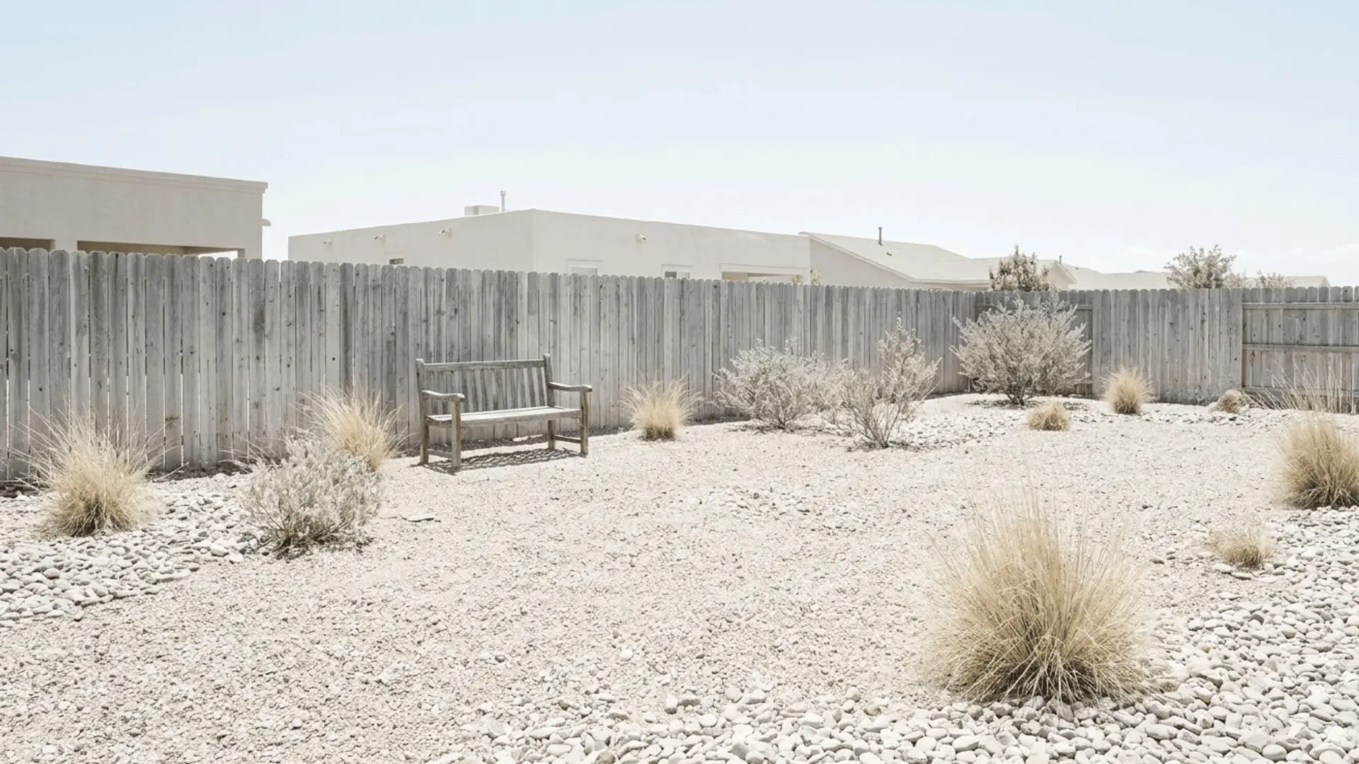 faded sun-bleached desert backyard with pale washed-out gravel sparse plants and colorless weathered wooden fence