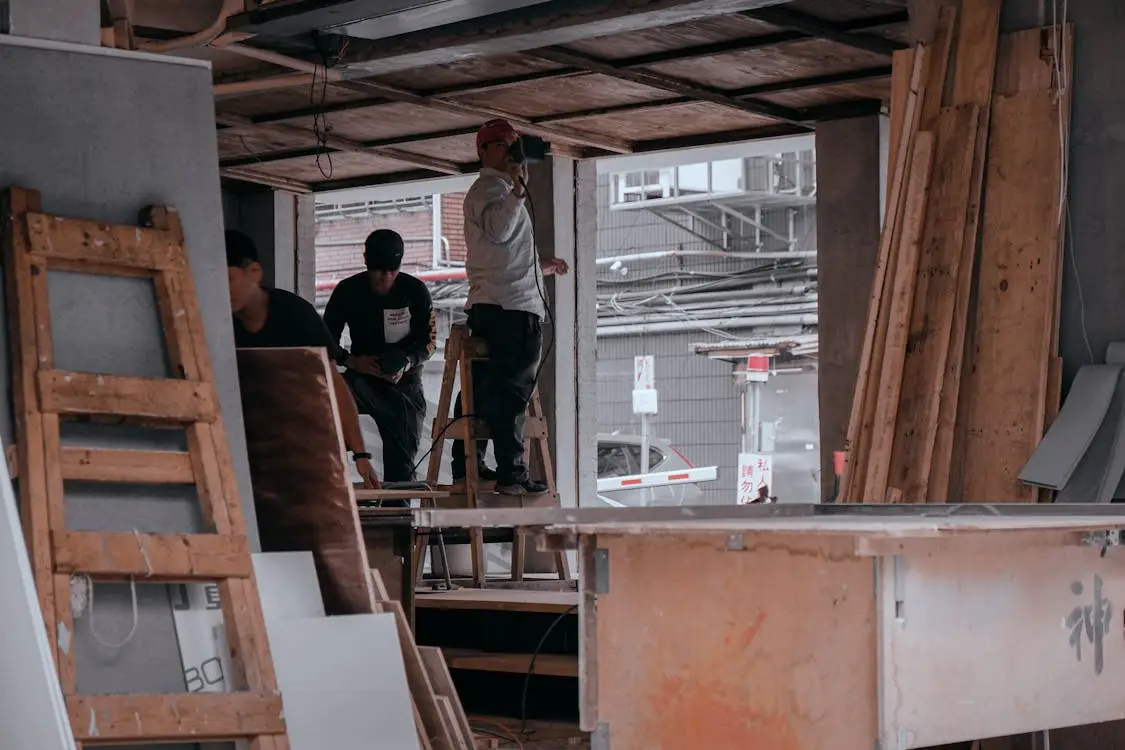Construction workers in partially built structure with wooden planks and tools in dimly lit setting