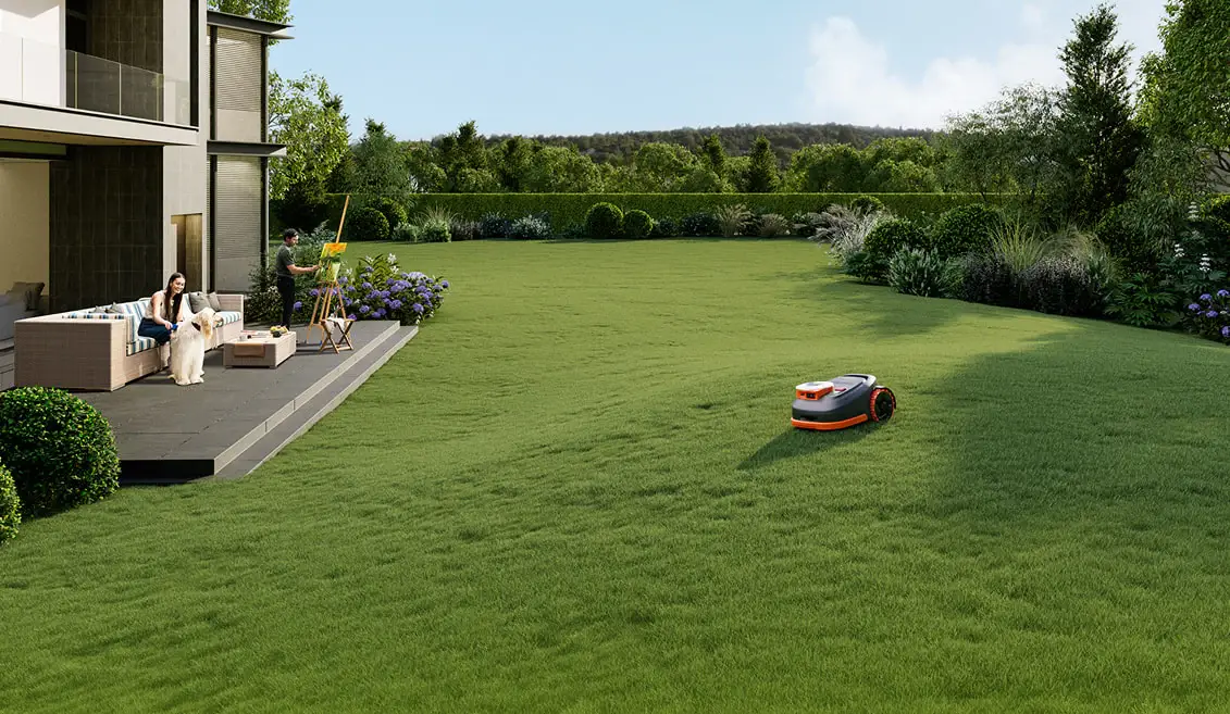 Robotic lawnmower on green lawn with person painting and woman with dog on patio