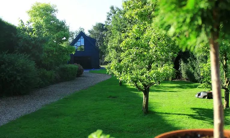Lush green garden with trees and gravel path leading to dark blue house