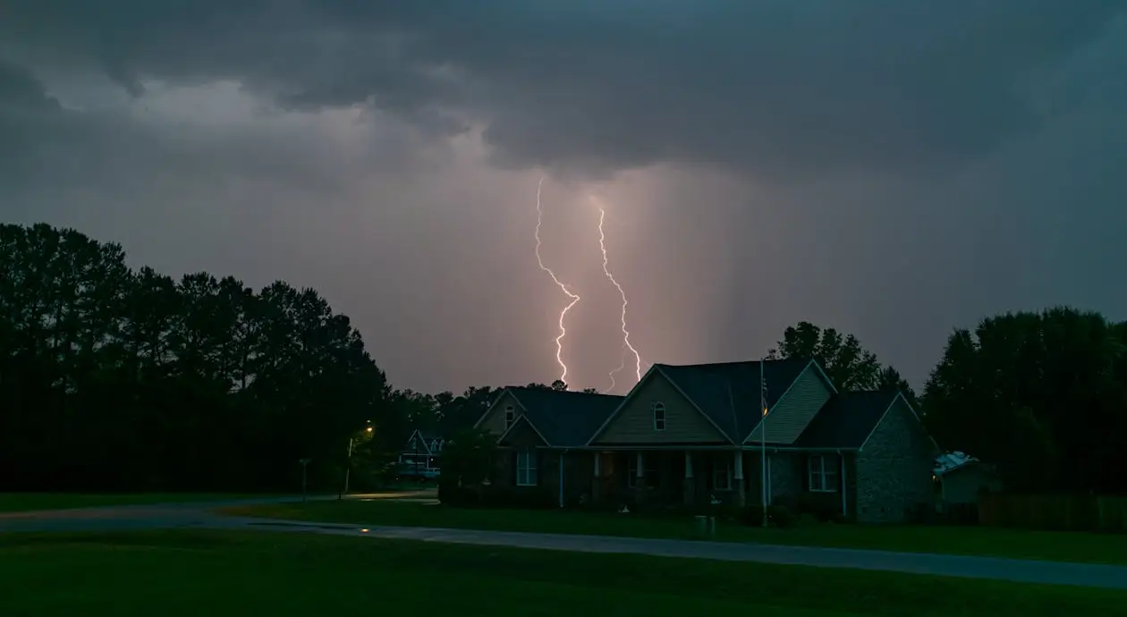 Lightning striking behind suburban house under dark storm clouds at night.