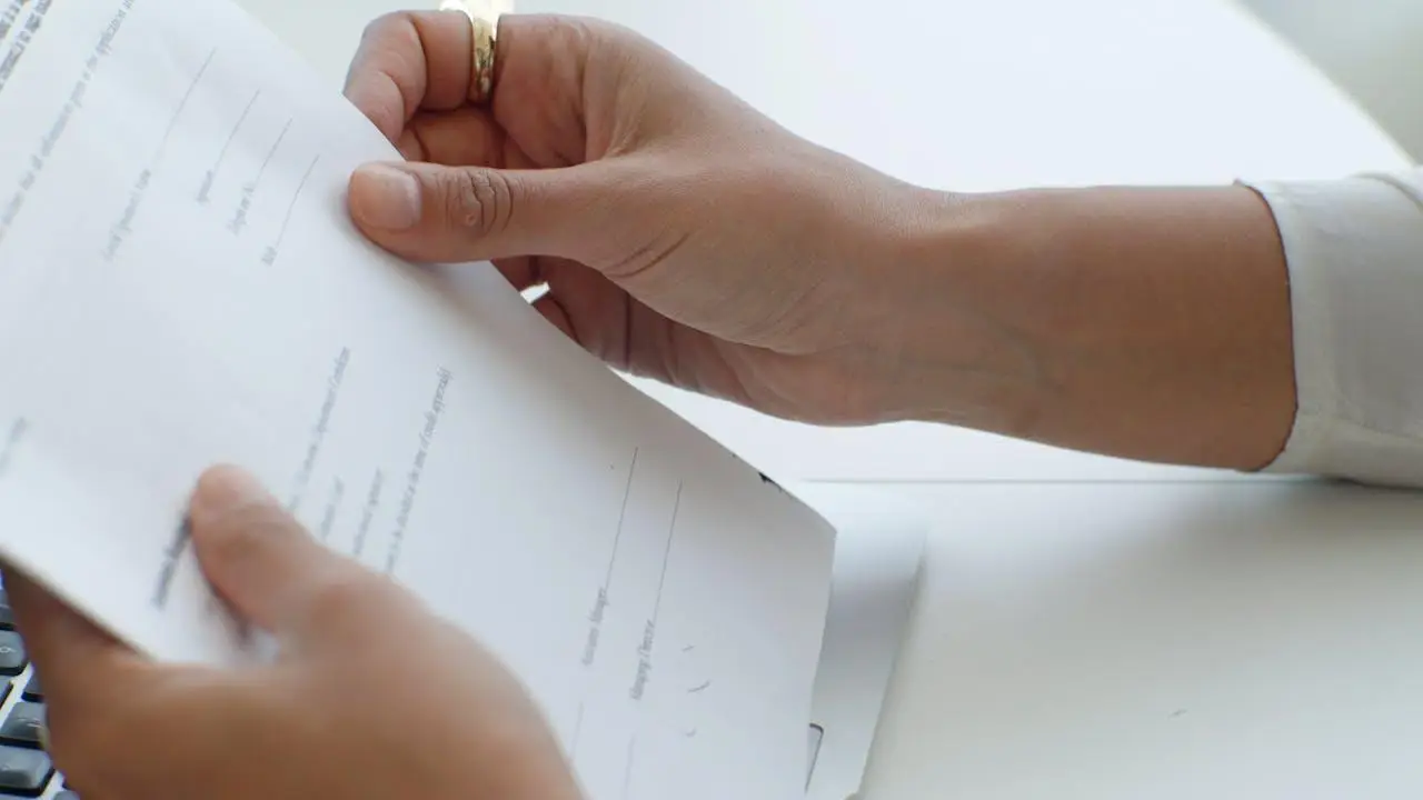 Hands holding a document over a white desk beside a keyboard