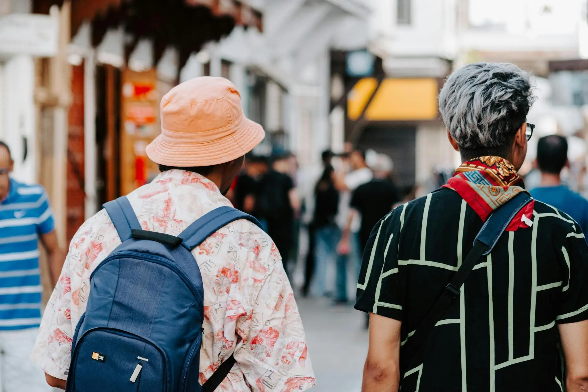 Two people walking in a bustling street wearing casual clothing and backpacks