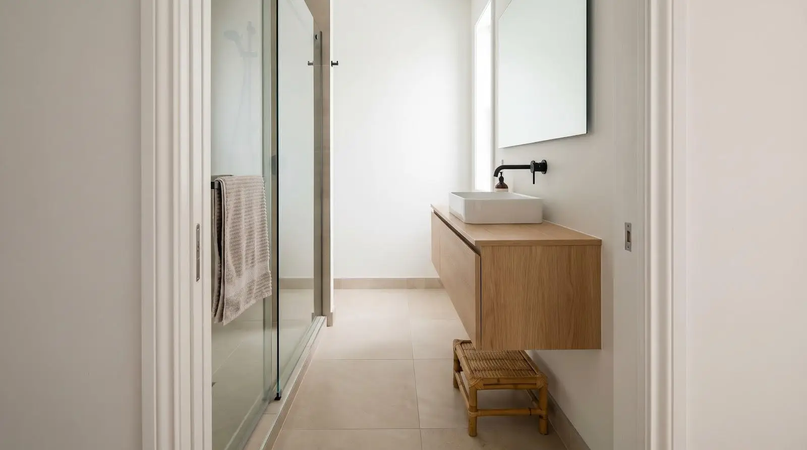 Minimalist bathroom with wooden floating vanity, vessel sink, and glass shower doors