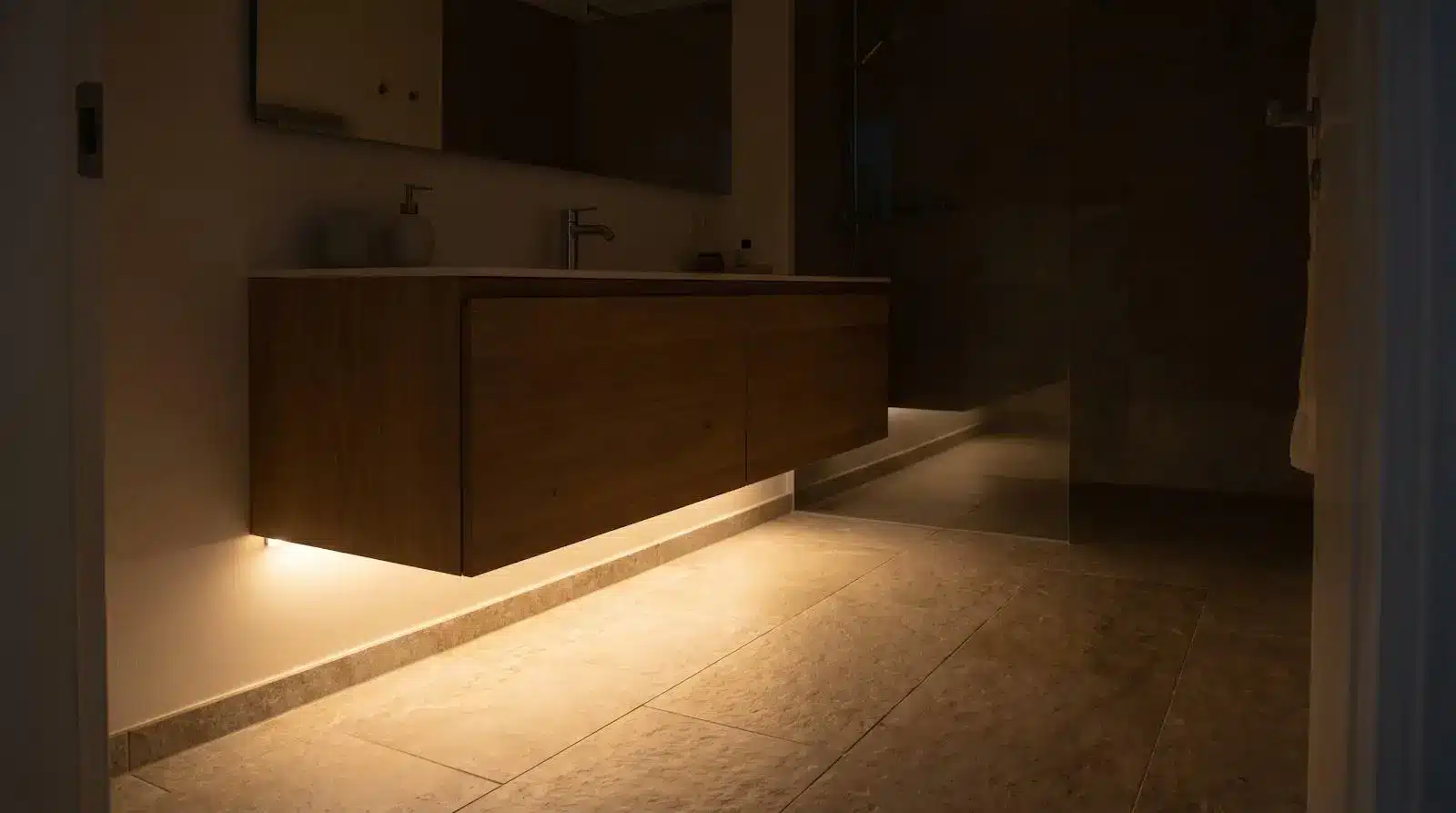 Floating wooden bathroom vanity with underlighting in dimly lit modern bathroom