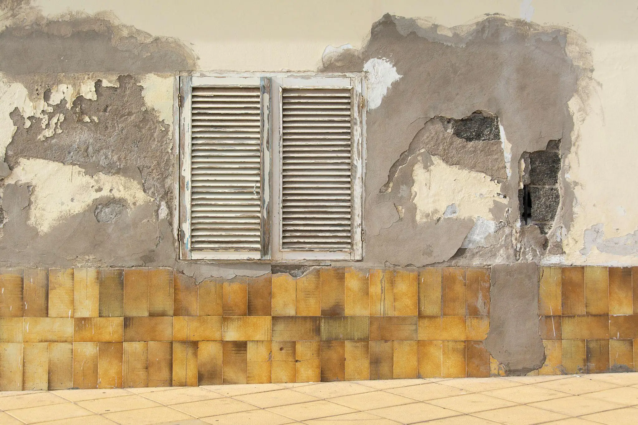 Peeling plaster wall with weathered wooden shutters above brown tiles