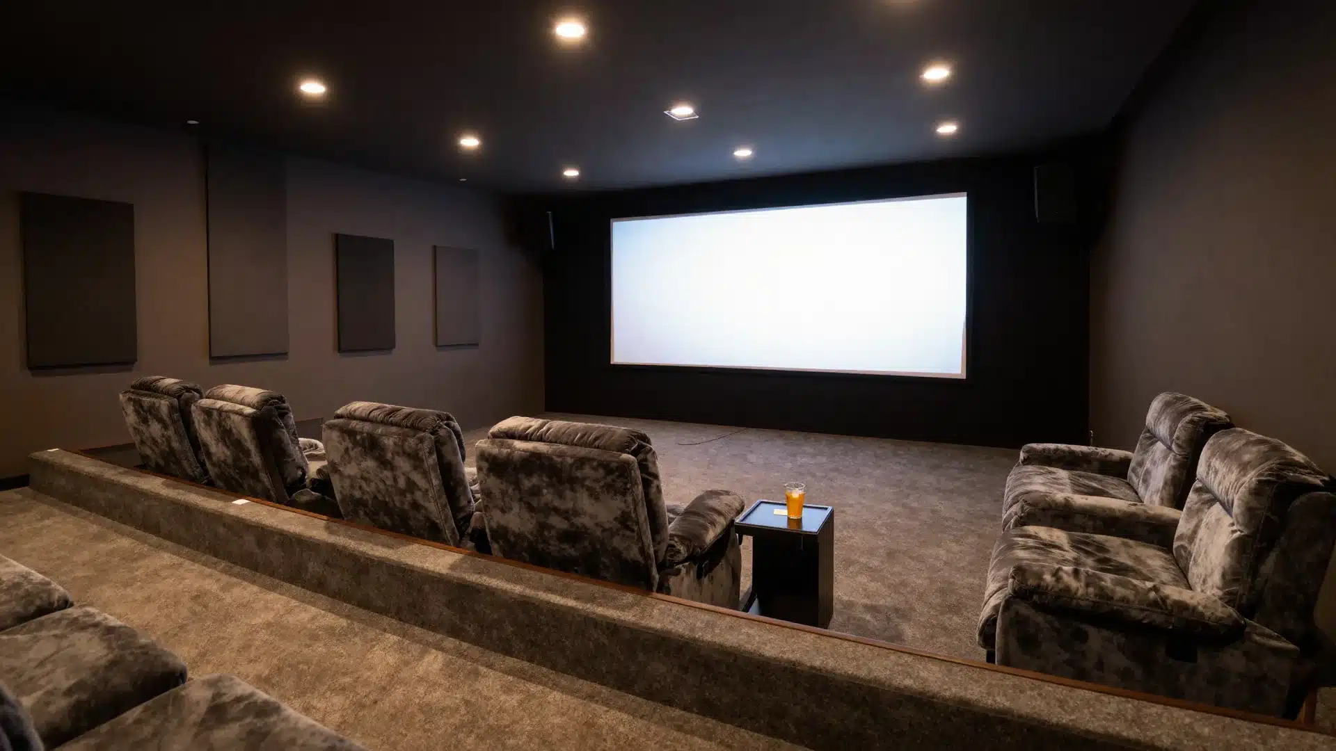 A dark, cozy home theater with a large screen, tiered plush seating, and soft ambient lighting for a cinematic experience
