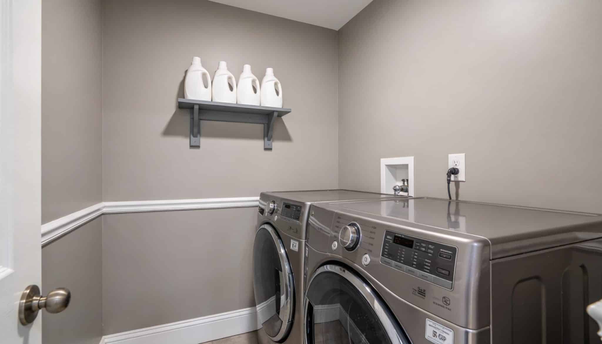 A modern laundry room featuring light gray walls, white trim, and stainless steel appliances.