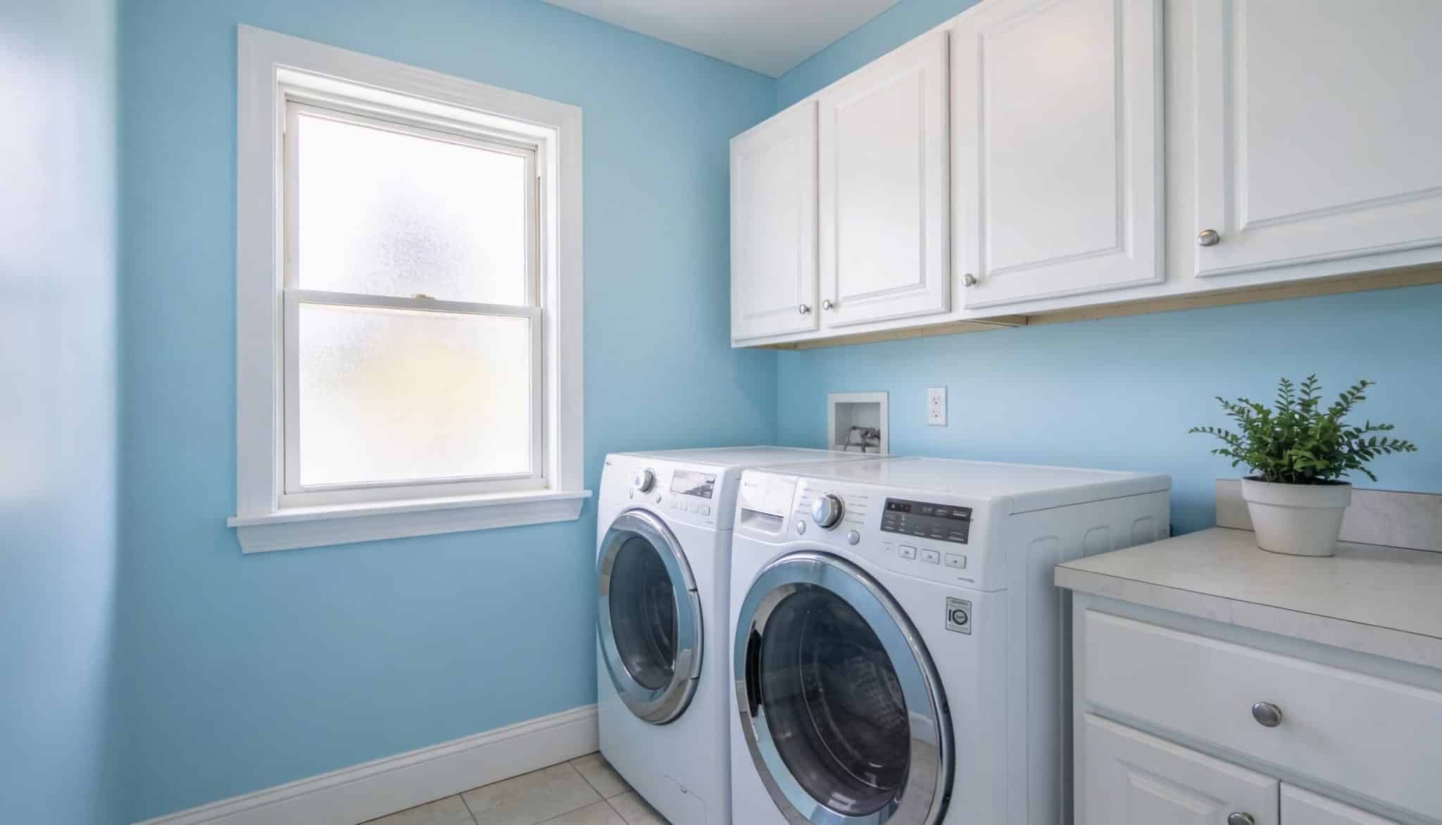 Laundry room painted in a light, airy sky blue, featuring clean white shelving and bright lighting.