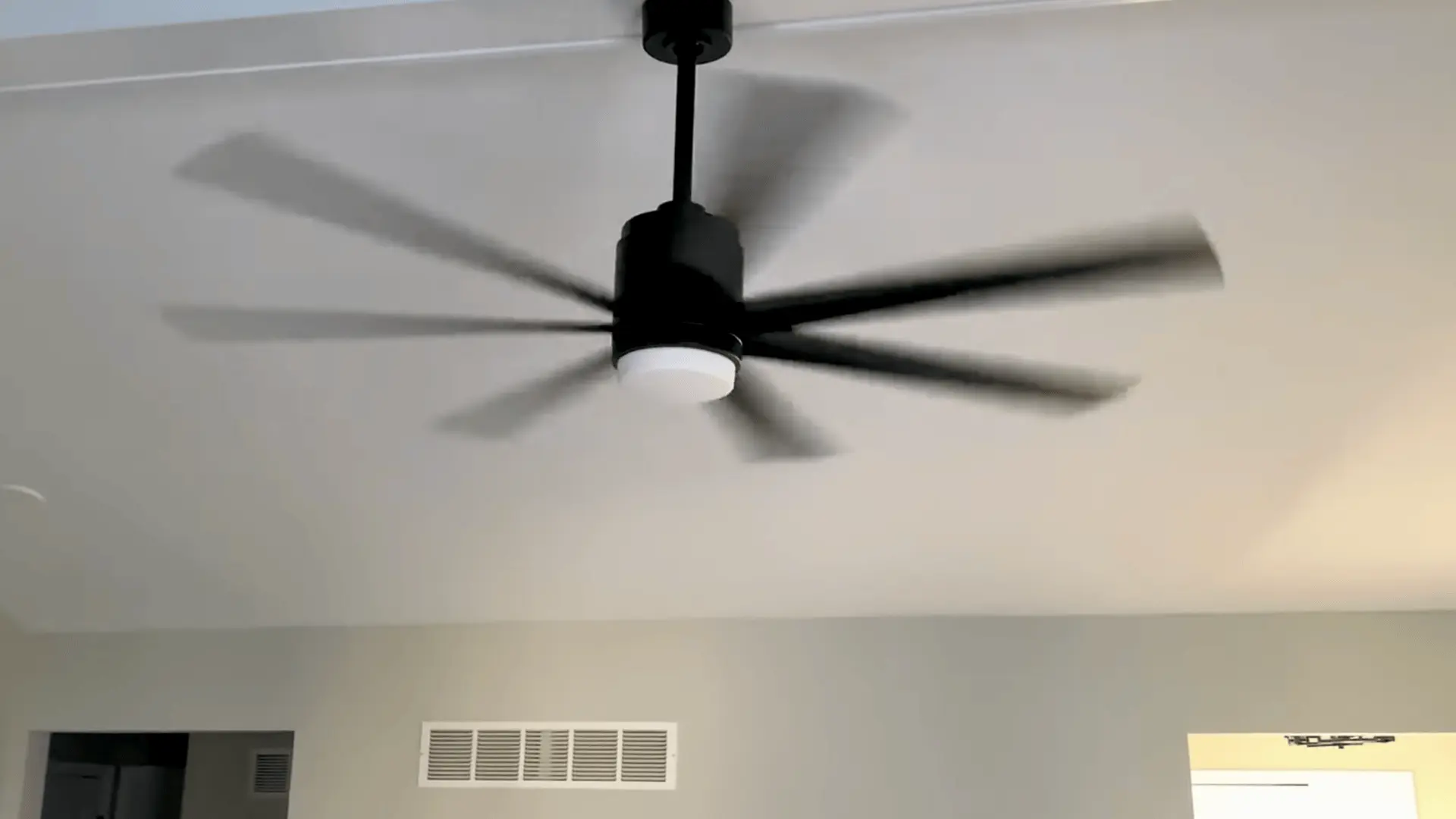 a black ceiling fan with multiple blades spinning in a bright white room