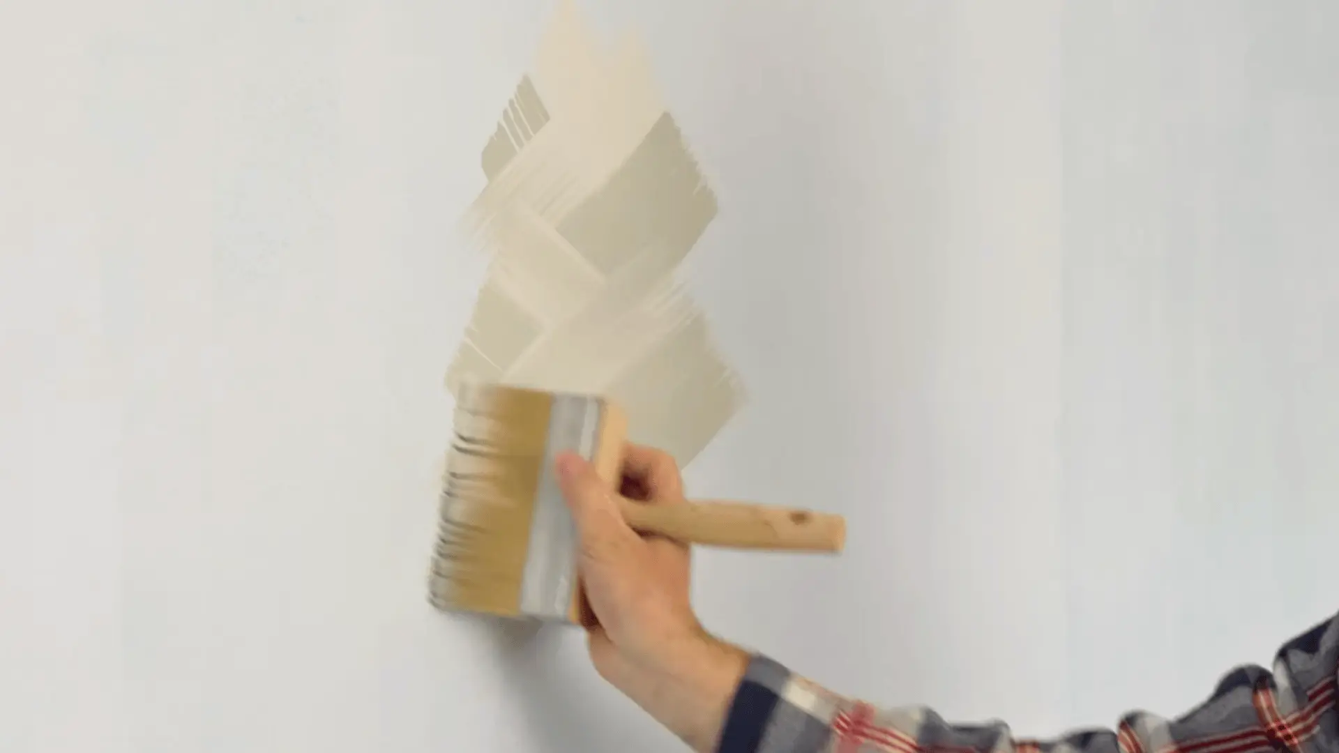 a hand applying limewash paint on a wall using x-pattern brush strokes for a soft textured finish
