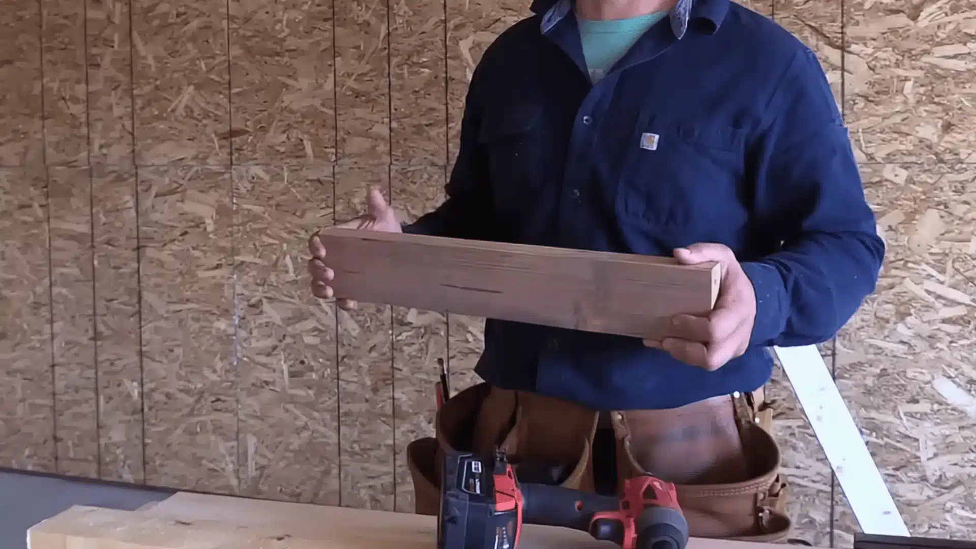 a person holding a wooden 2x4 board for diy garage shelf construction with a drill placed nearby