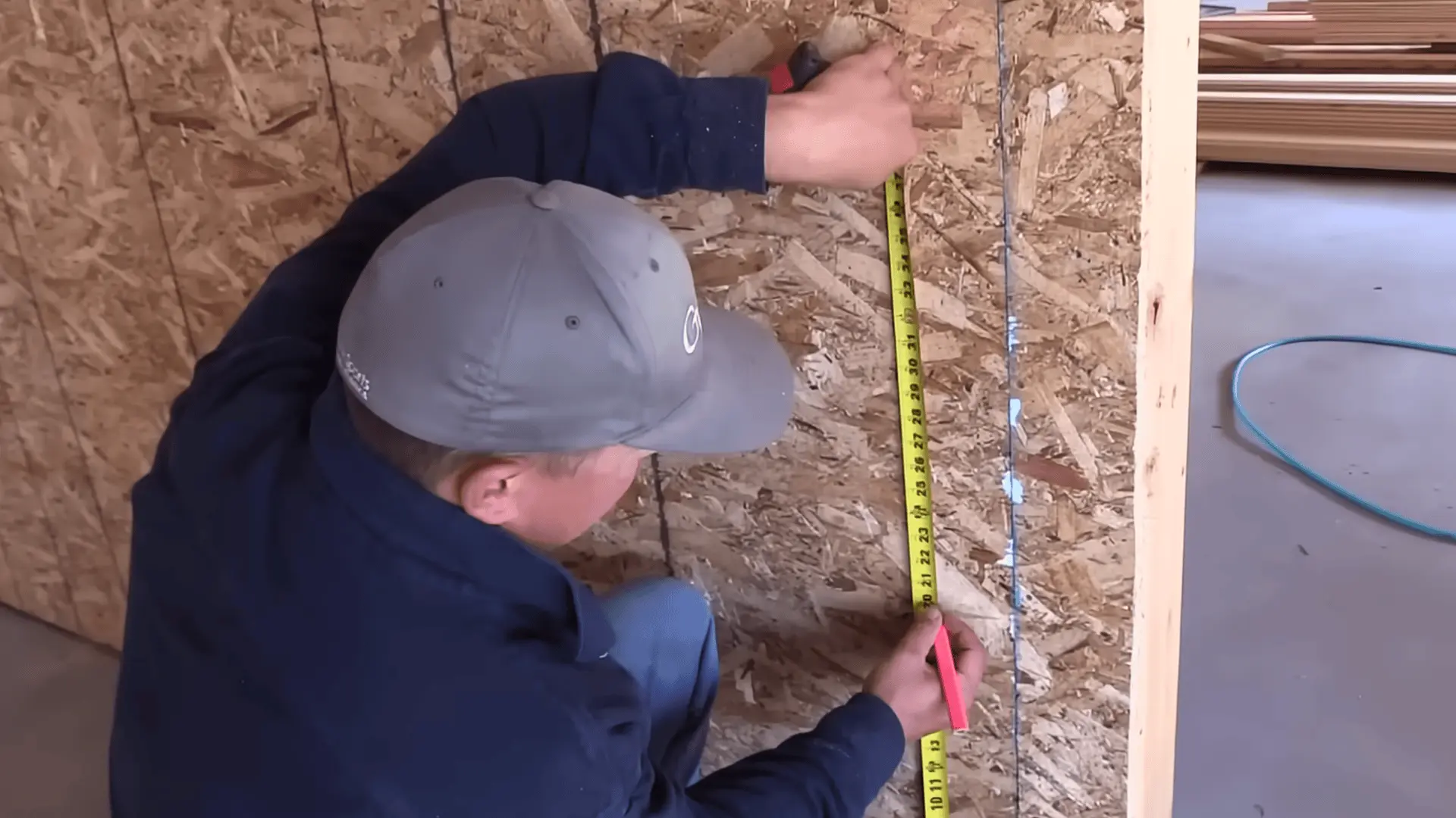 a person measuring and marking wall height with a tape measure for diy garage shelf installation
