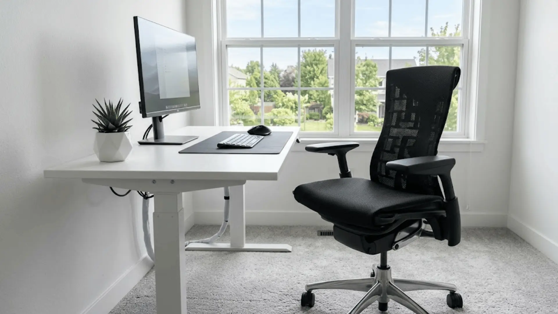 black mesh ergonomic office chair at a minimal white desk in a clean home office with natural daylight