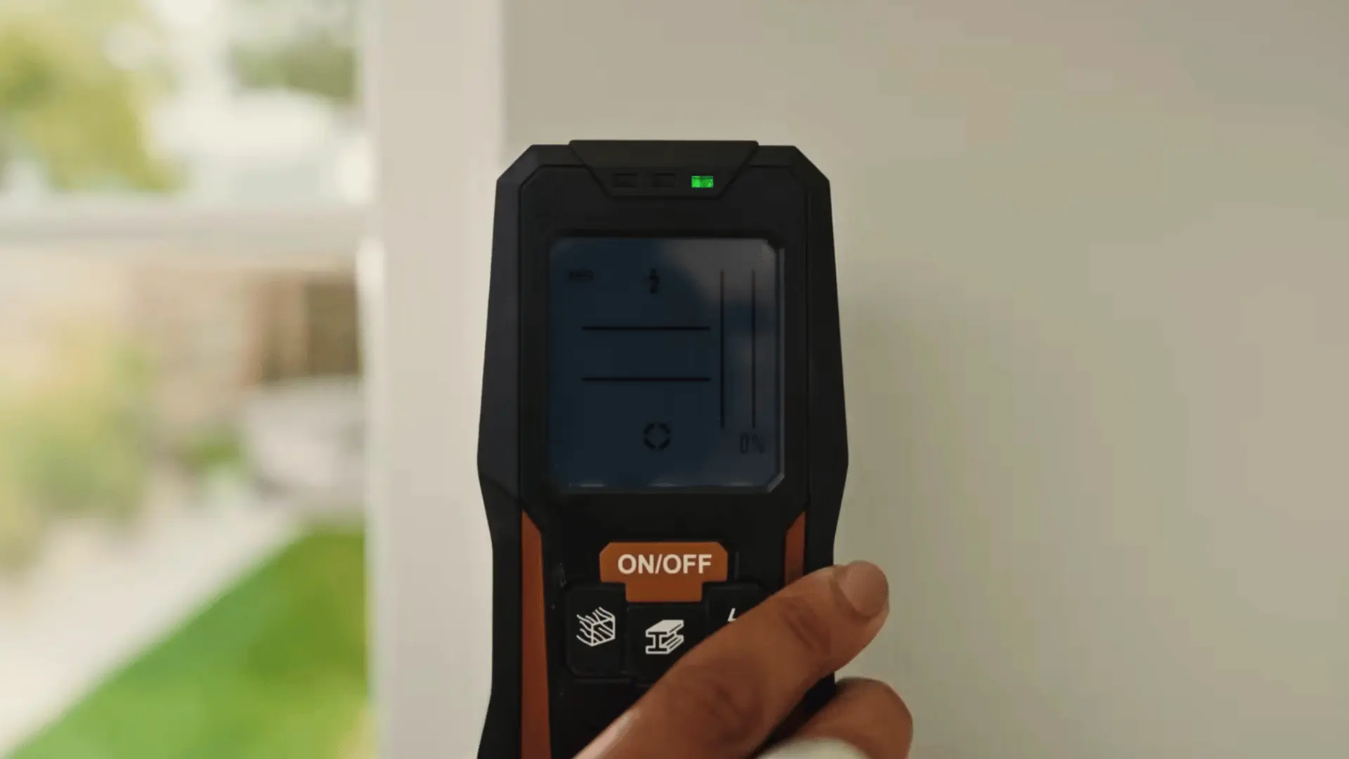 hand holding a stud finder against a drywall surface to detect studs before drilling