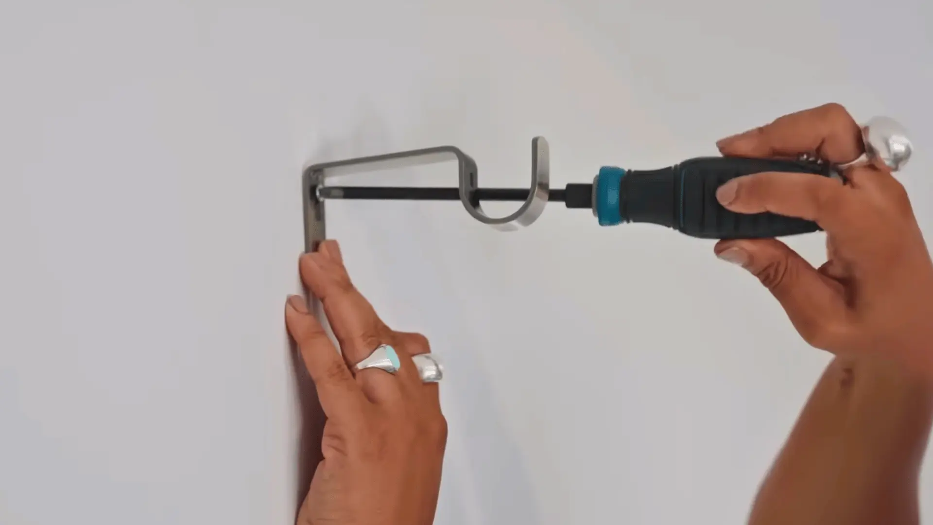 hands securing a curtain rod bracket to the wall using a power drill