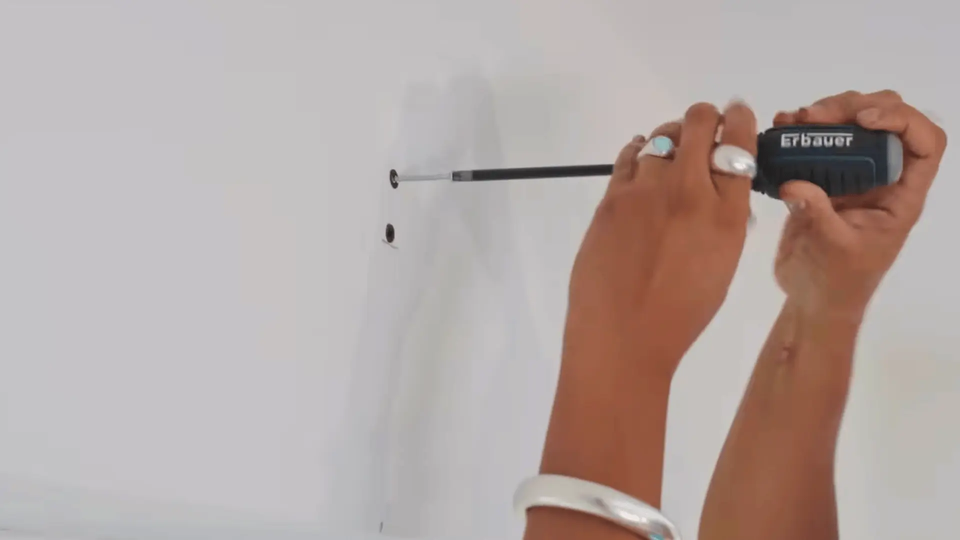 hands using a power drill to drive a screw into a predrilled wall hole for curtain rod bracket installation