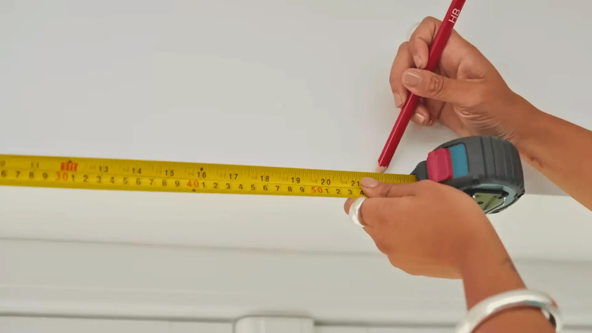 person measuring wall with tape measure and marking with pencil for curtain rod bracket placement