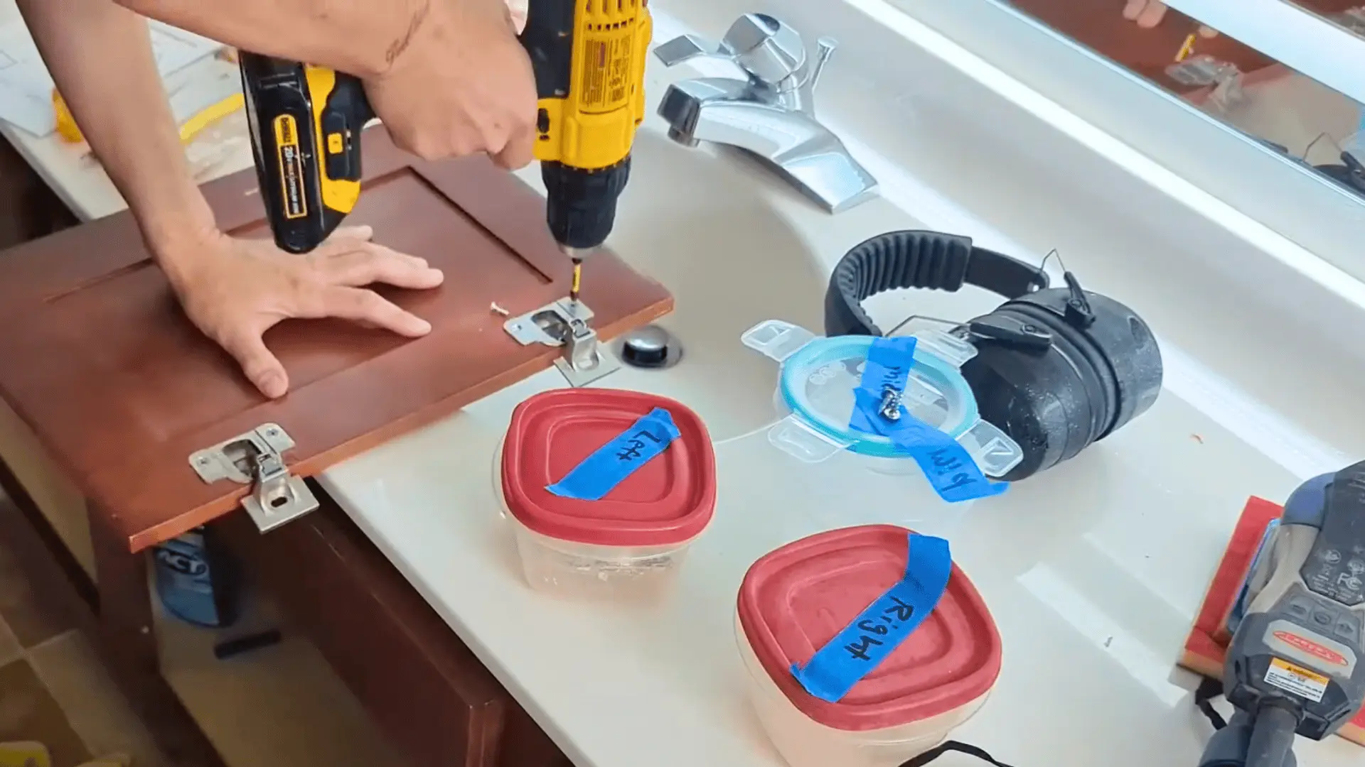 person removing cabinet door hinges with a drill, with labeled containers for hardware organization