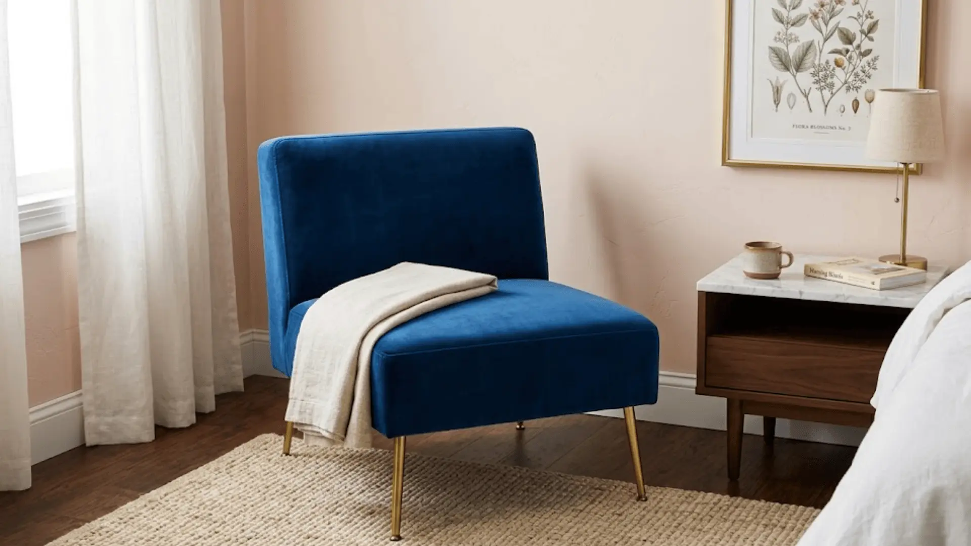 sapphire blue velvet slipper chair with gold legs beside a marble nightstand in a blush-toned bedroom