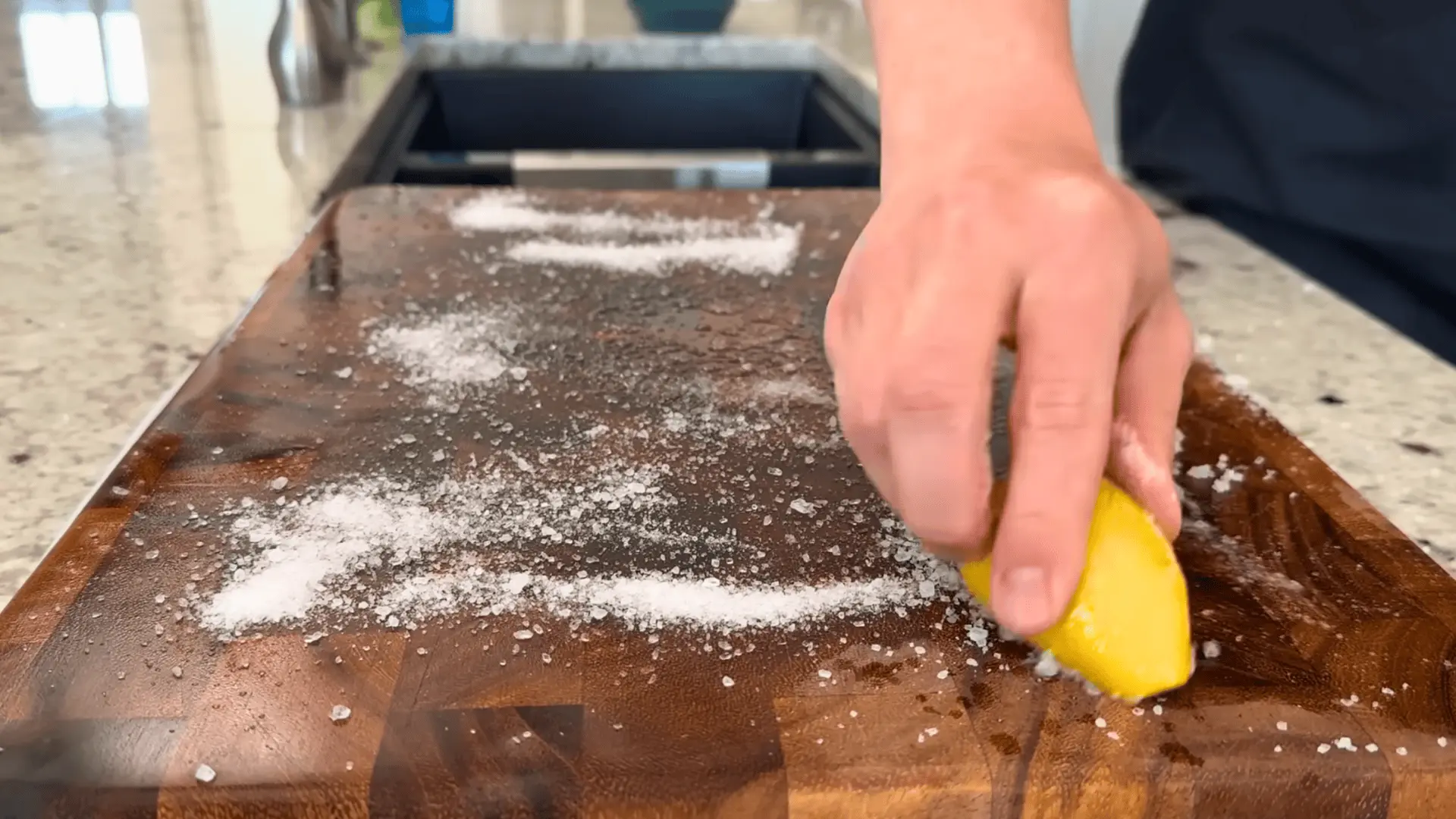 scrubbing a wooden cutting board with coarse salt and a halved lemon to remove odors and bacteria