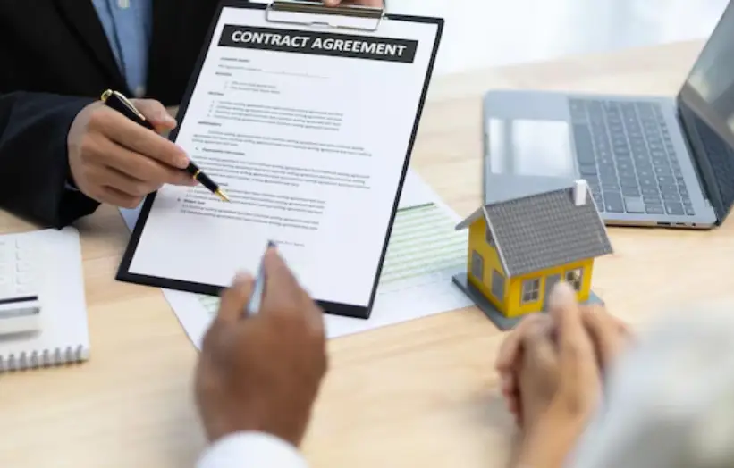 Contract agreement discussion on wooden desk with miniature house and laptop nearby
