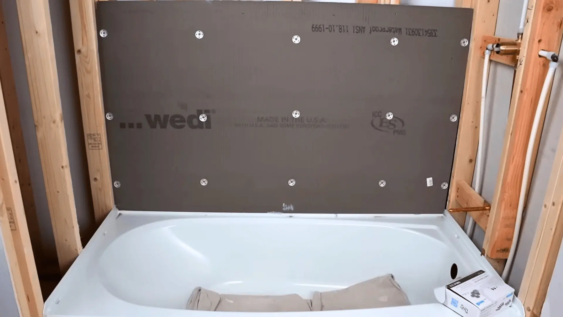 waterproof foam backer board screwed into shower wall studs above a white bathtub during renovation