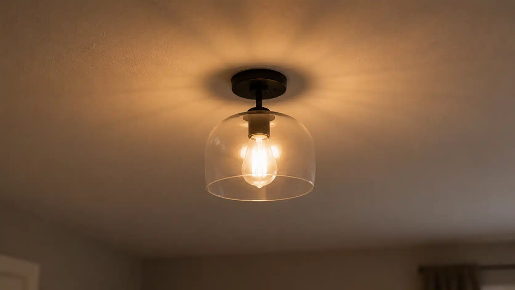 a warm amber light bulb in a clear glass fixture mounted on a ceiling, casting a soft glow in the room