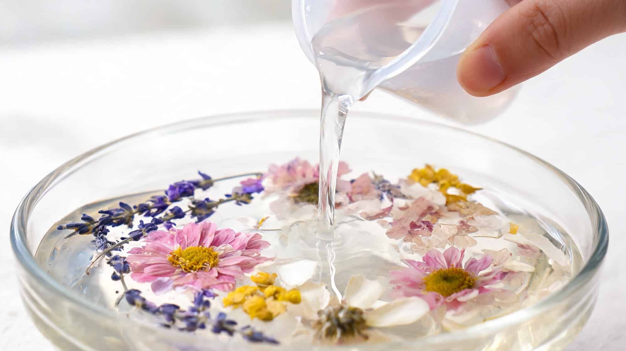 how to preserve flowers hand pouring liquid into bowl with colorful flowers floating in water