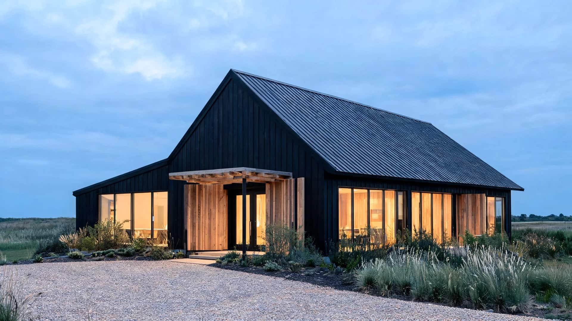 black metal and wood modern farmhouse exterior barn style with gable roof and warm lit interiors at dusk