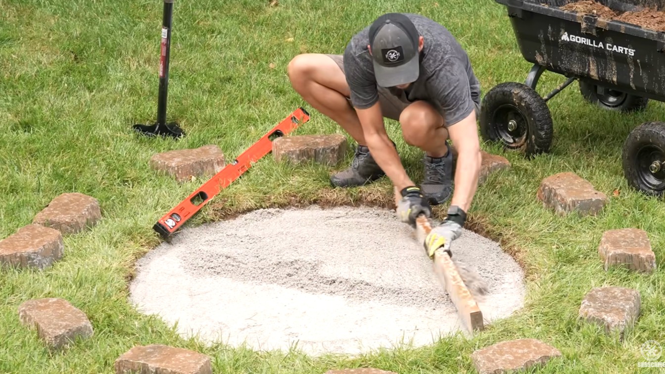 diy backyard ideas with a builder leveling the paver base before stacking stone blocks in a circle shape