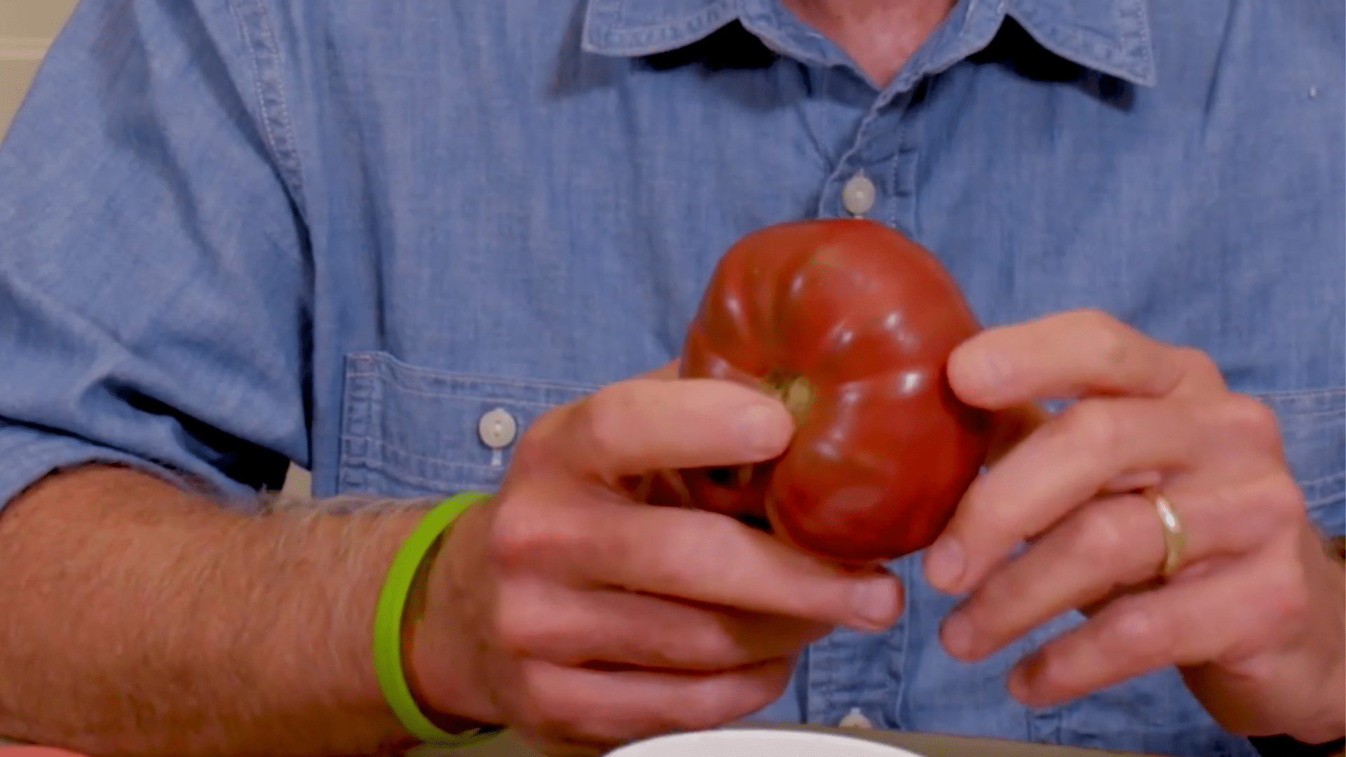 ripe tomato being cut open with seeds scooped into jar ready for seed saving process