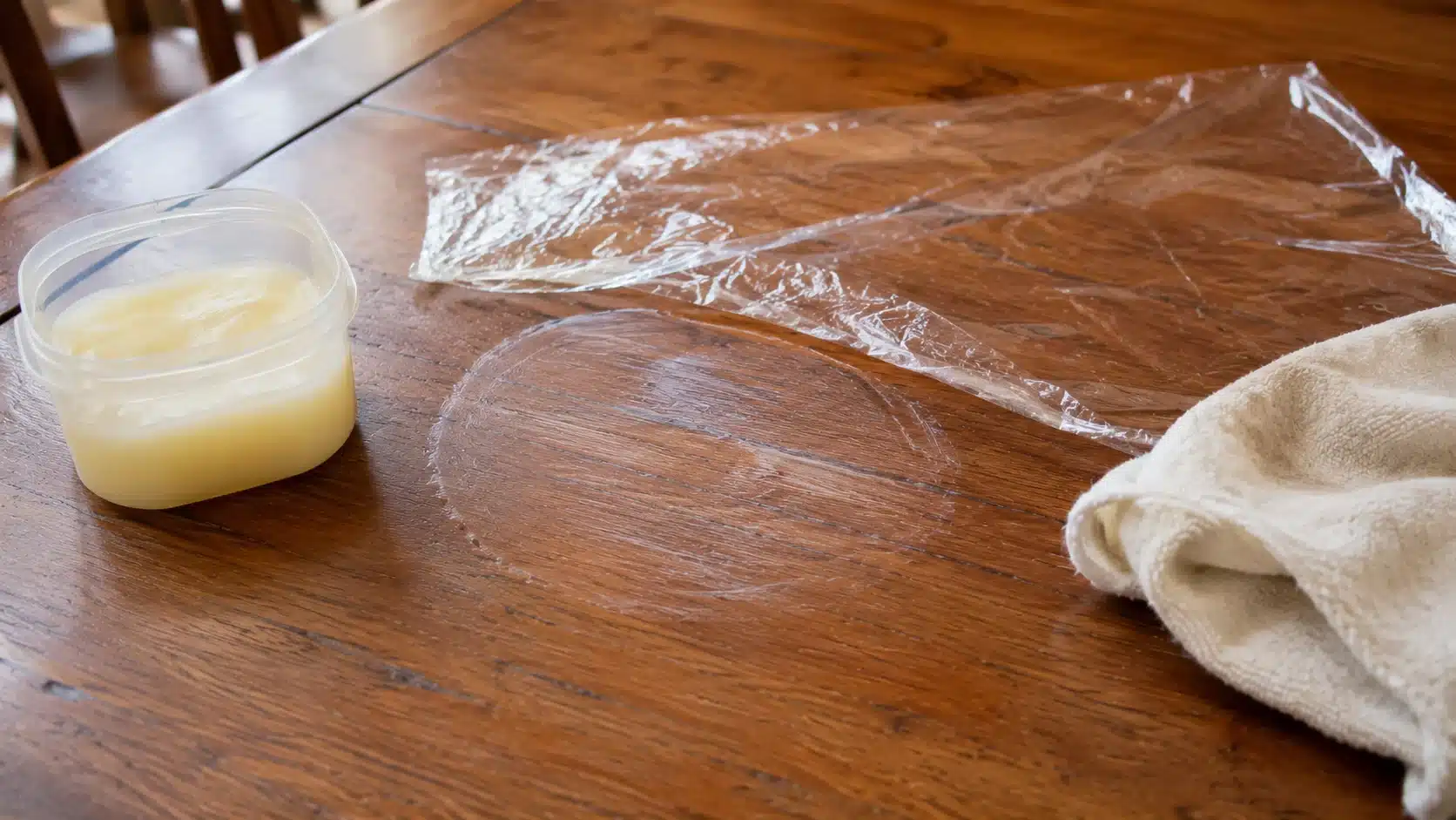 container of petroleum jelly beside cloth on wood table demonstrating how to remove water stains from wood at home