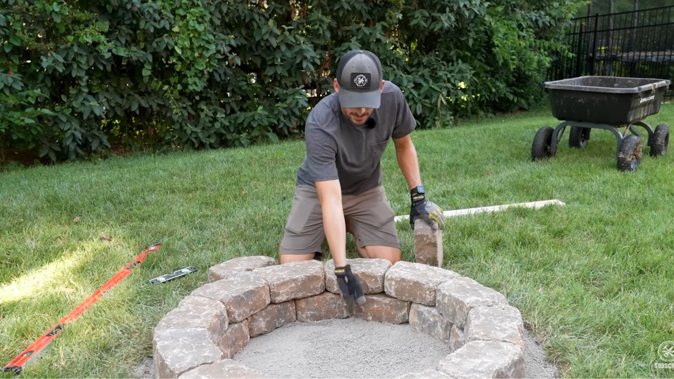 diy backyard ideas showing stone blocks being adjusted for a clean round fire pit shape on grass