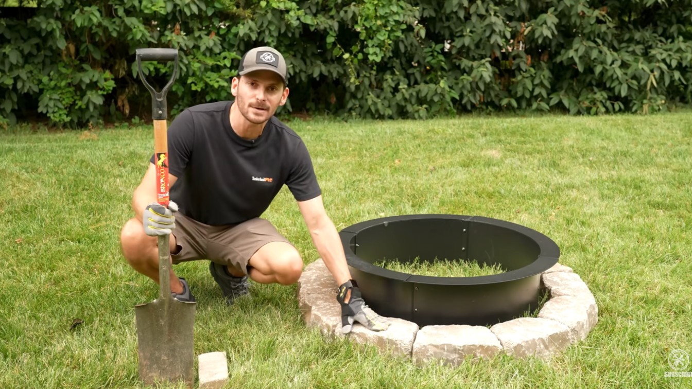 diy backyard ideas with first stone blocks placed around a metal fire pit ring on a green backyard lawn
