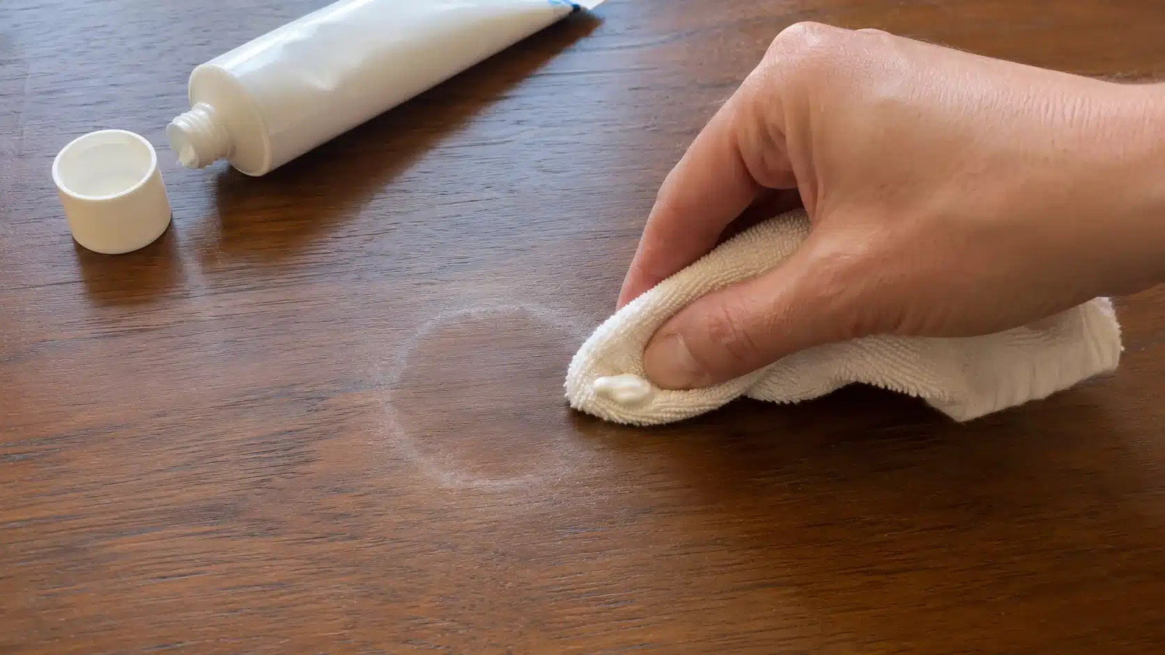 hand applying toothpaste to a wood table to demonstrate how to remove water stains from wood safely at home