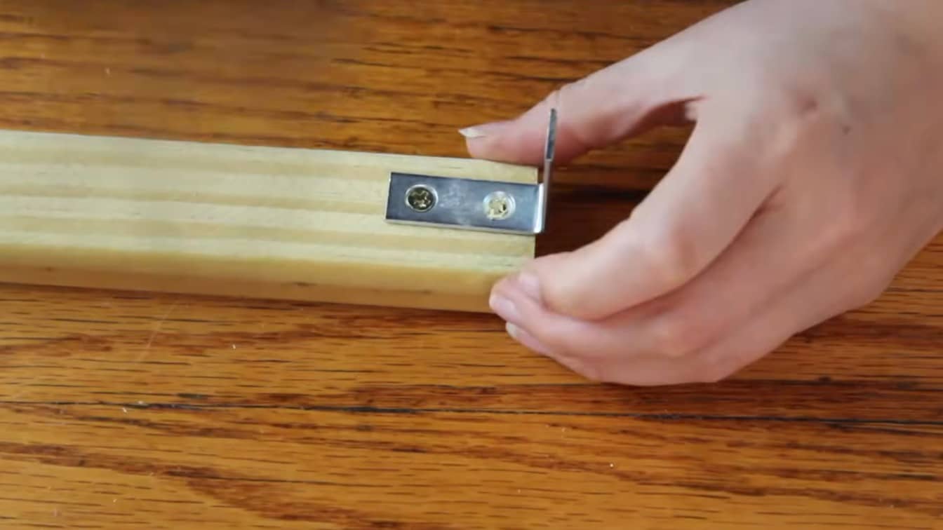 hand attaching a metal angle bracket to a wood strip for roman shade mounting hardware at home
