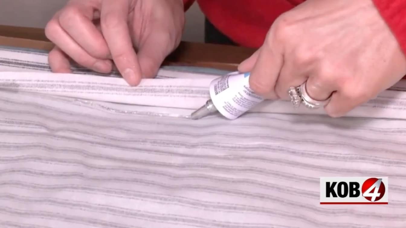 hands applying fabric glue to striped fabric edge for a diy roman shade made from mini blinds