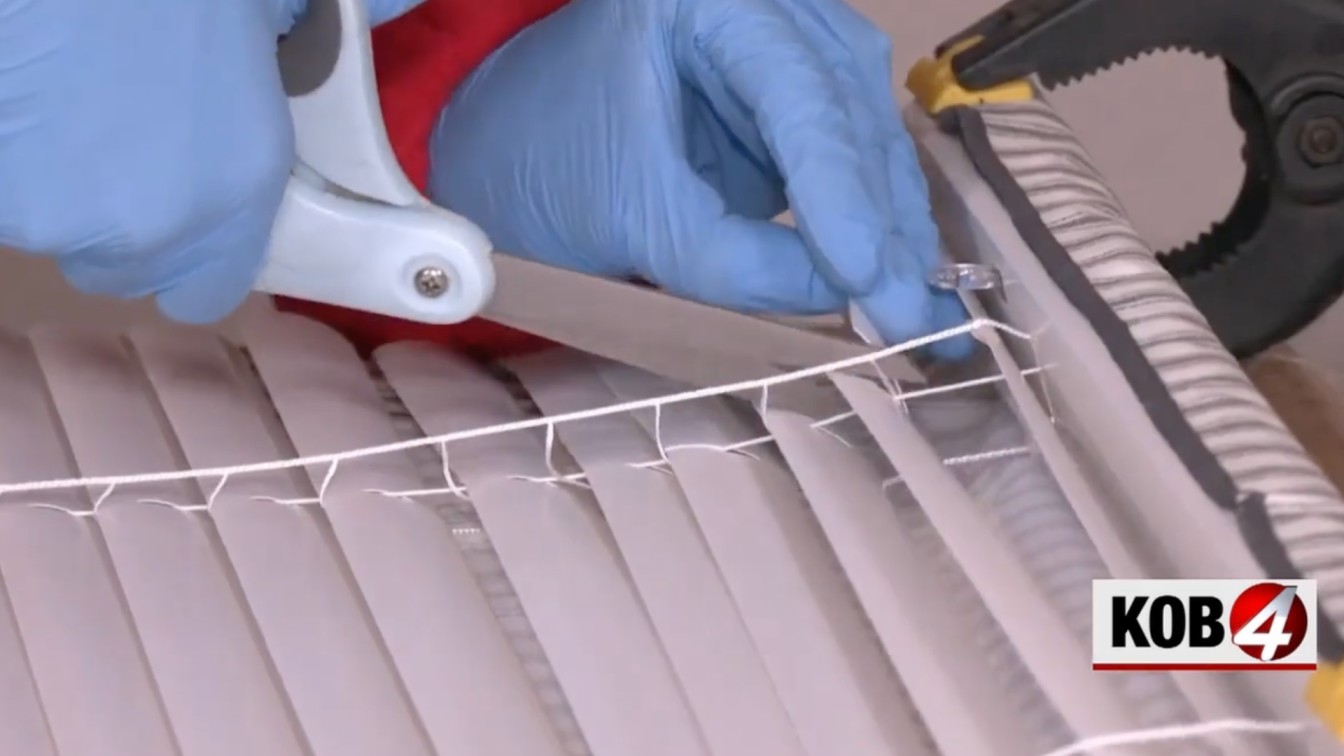 hands cutting ladder strings from mini blinds for a diy roman shade window project at home