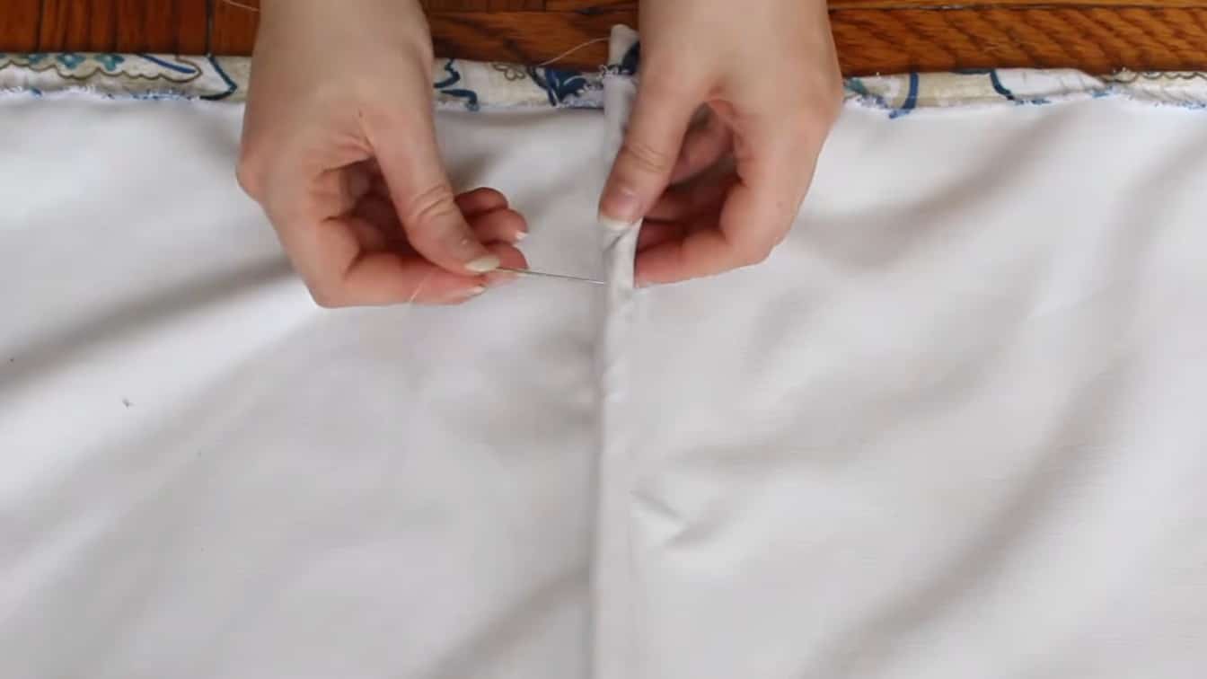 hands sewing a small plastic ring onto white lining fabric for a roman shade cord system at home