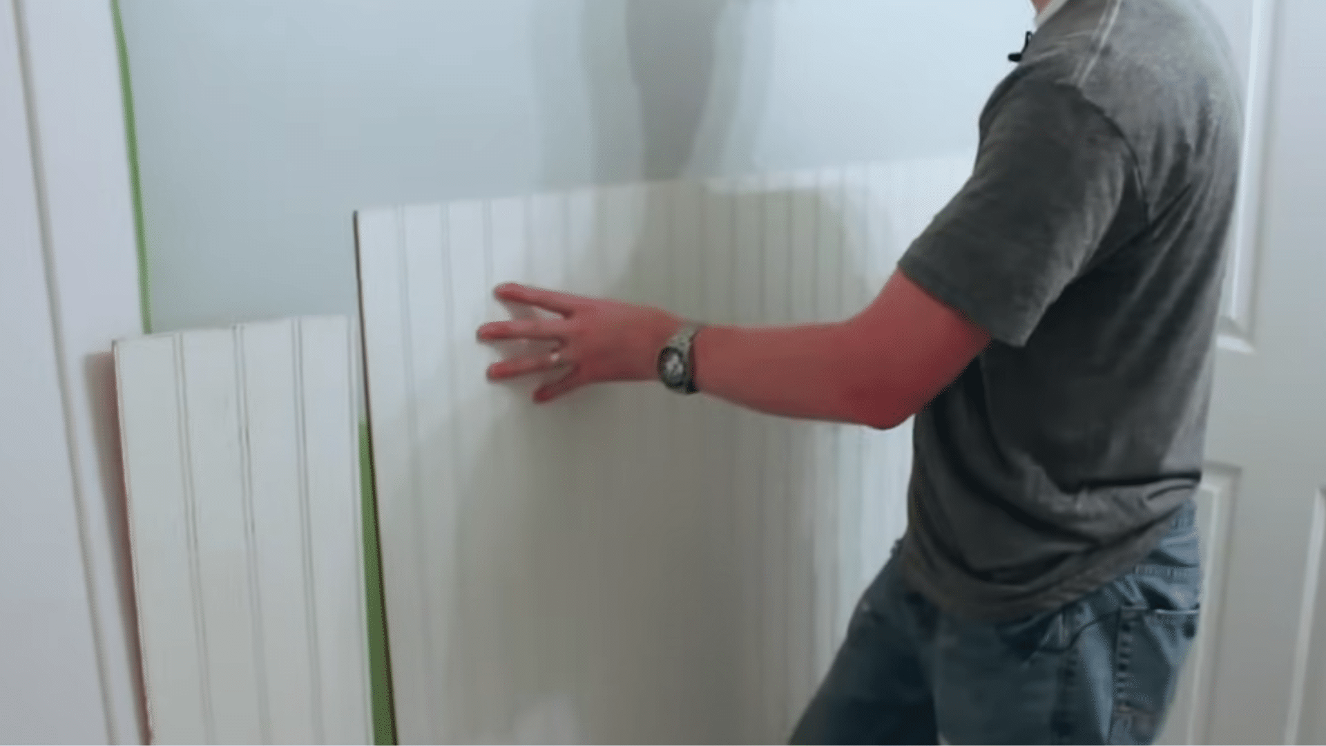holding a cut beadboard panel against the wall to check the fit at the baseboard corners and top edge