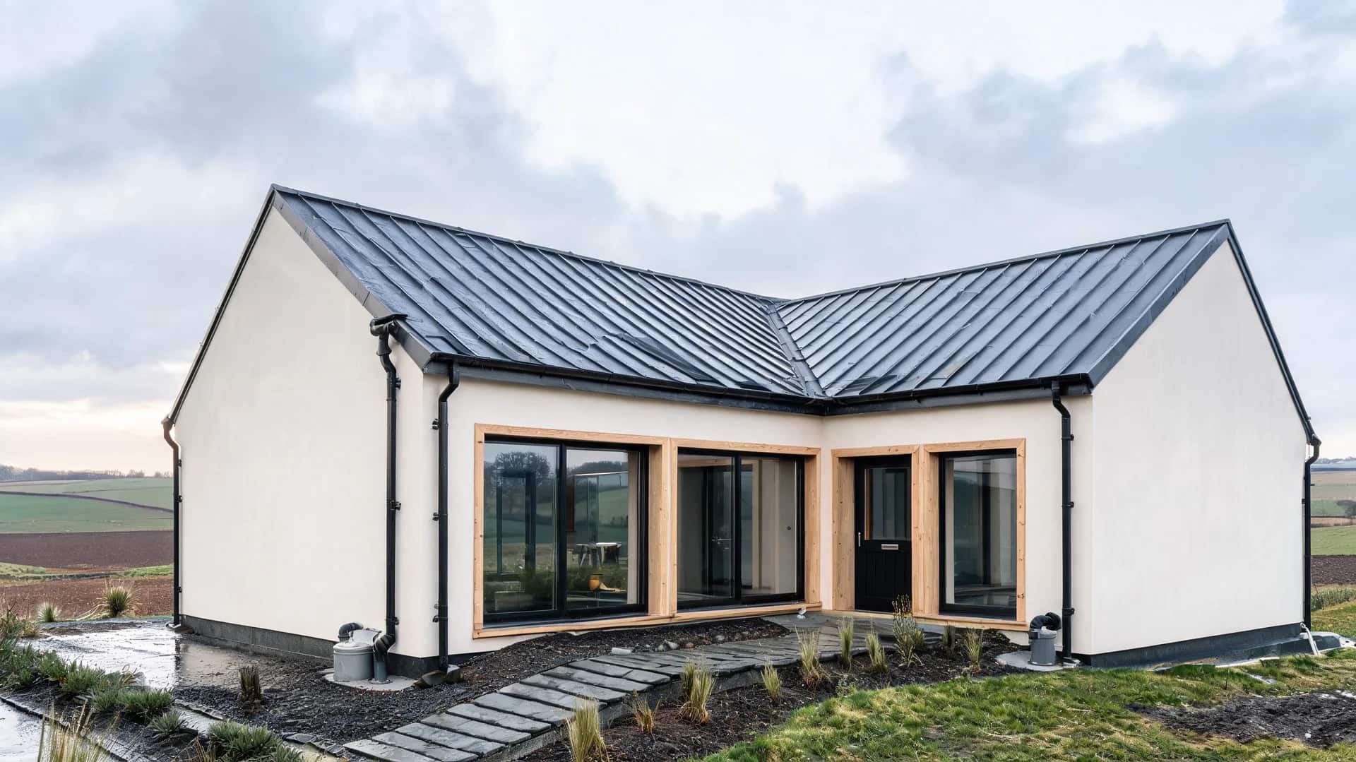 modern farmhouse exterior with rainwater harvesting roof system plaster walls wood accents and wet rural field surroundings