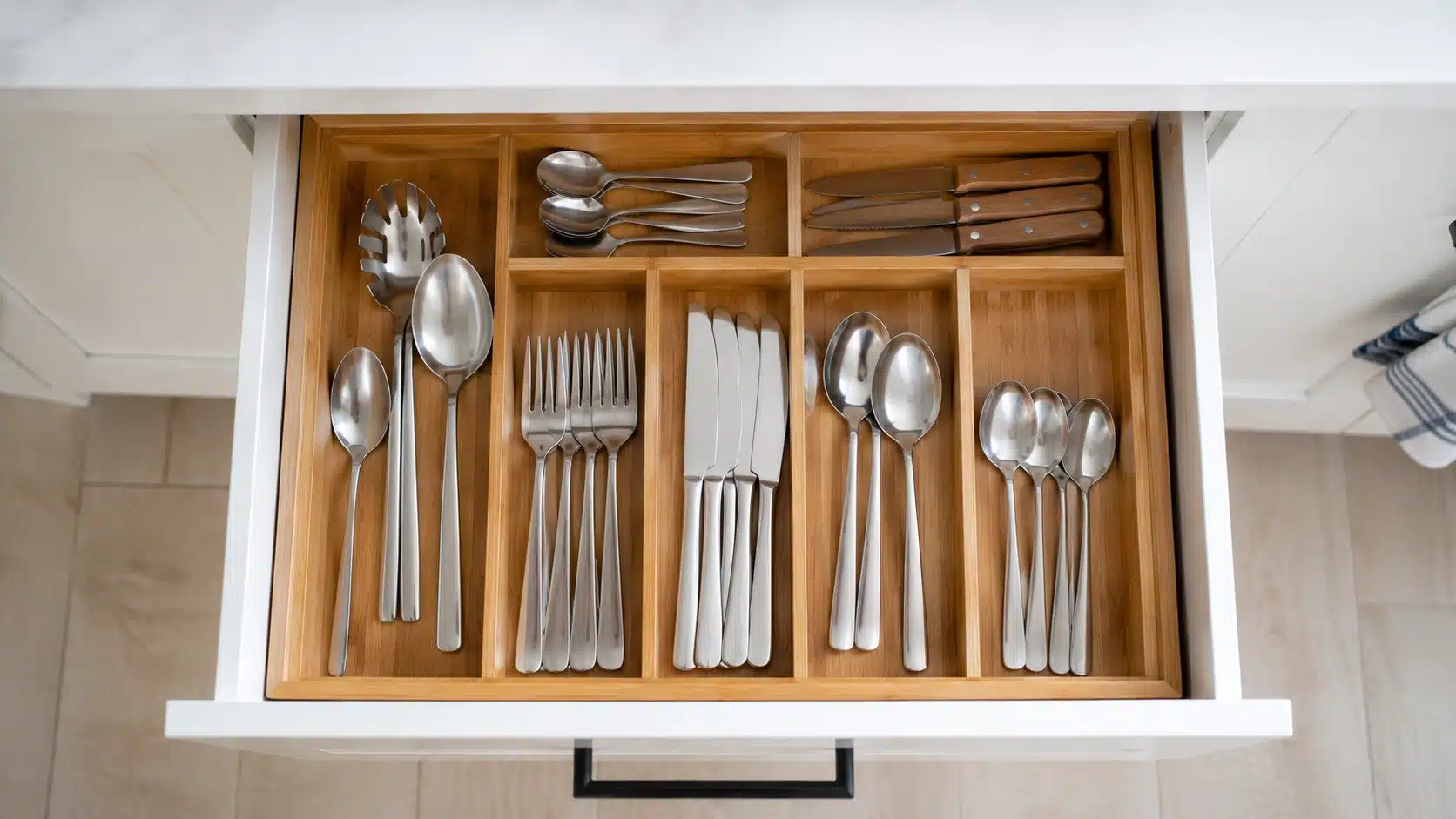 open drawer with bamboo organizer neatly separating silverware, knives, spoons, forks, and serving utensils in a kitchen