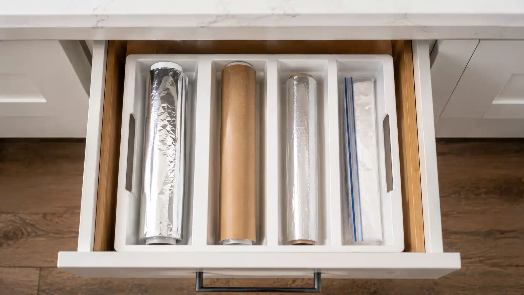 open kitchen drawer with white organizer holding foil, parchment paper, plastic wrap, and storage bags in separate slots