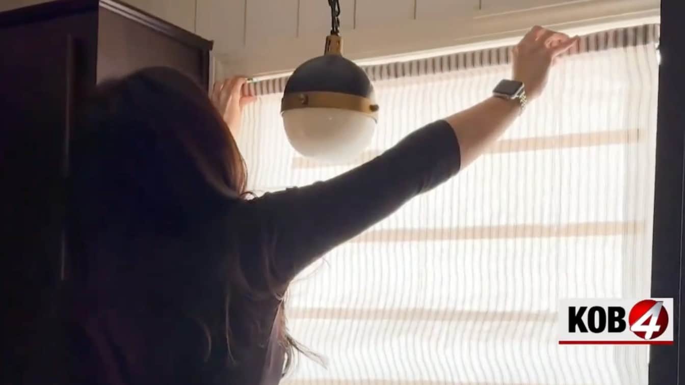 person hanging a finished diy roman shade made from mini blinds inside a bright home window