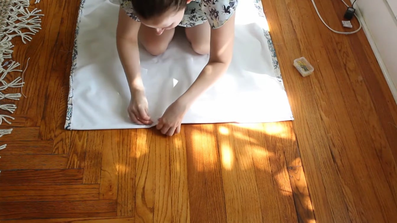 person measuring white lining fabric on a hardwood floor for a homemade roman shade project