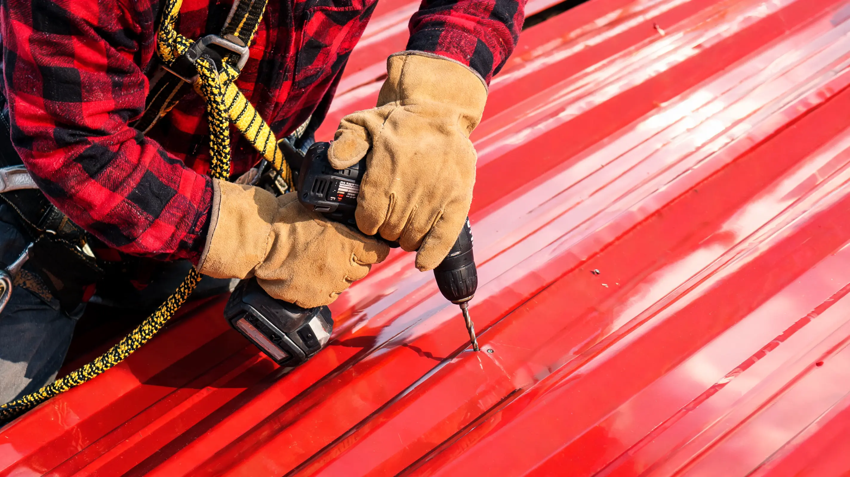 roofer handling metal roof maintenance by replacing screws on a red metal roof with safety gear